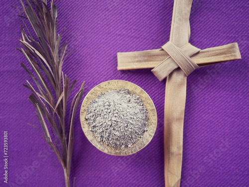 Christianity concept about Ash Wednesday, Good Friday, Lent Season and Holy Week. Dry palm leaf, Holy ash and a cross made of palm leaf arranged on purple background. photo