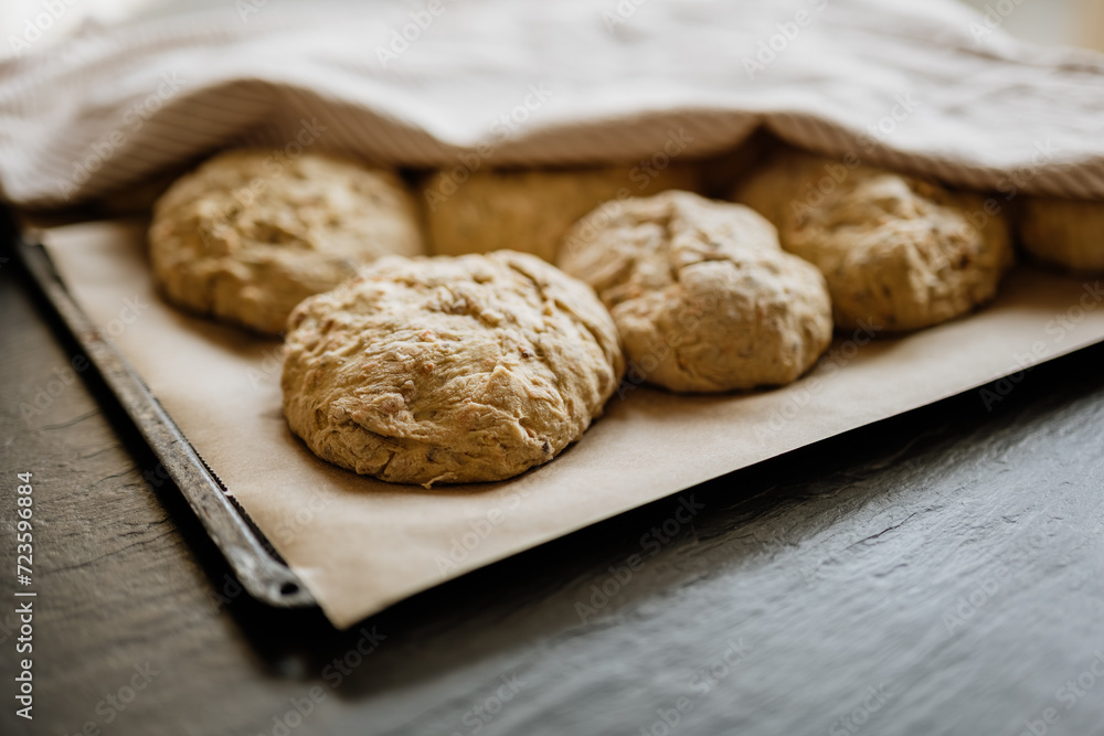 Baking bread at home and letting the dough rise. Buns on baking sheet covered with a kitchen towel ready to be baked in the oven. Baking bread at home and letting the dough rise. Buns on baking sheet covered with a kitchen towel ready to be baked in the oven.