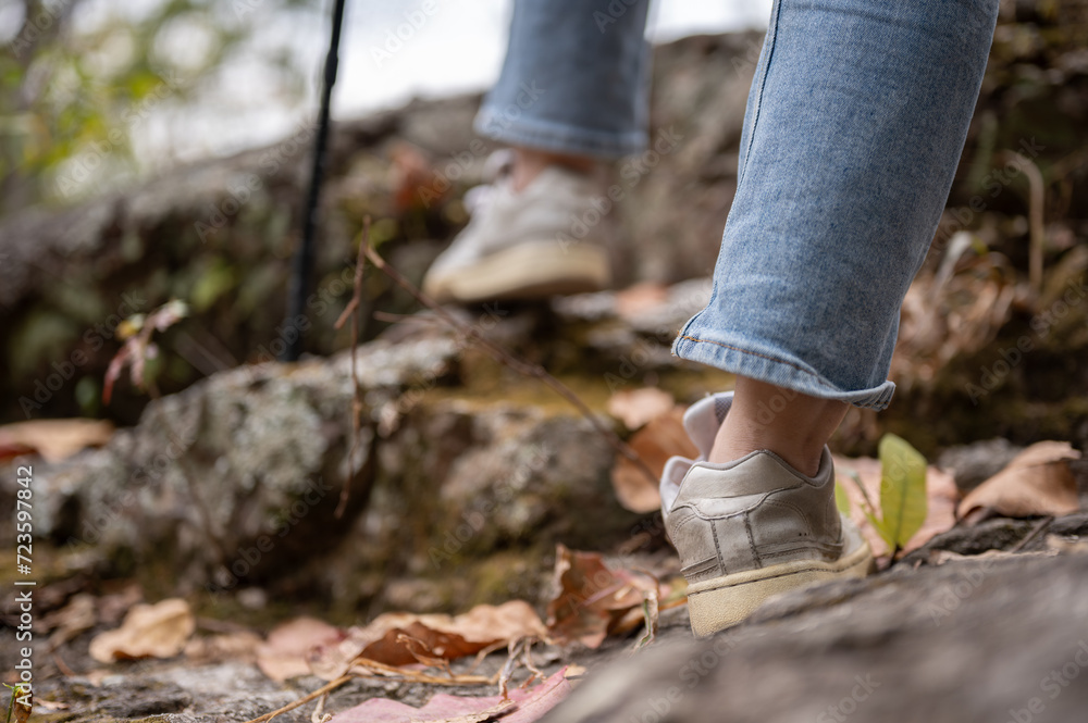 Close-up legs image of a woman is hiking with a trekking pole on the rock mountain. Close-up legs image of a woman is hiking with a trekking pole on the rock mountain.