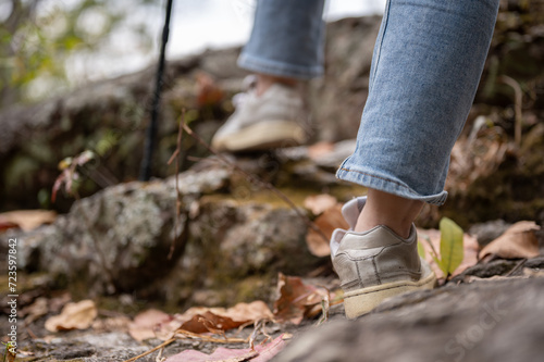 Close-up legs image of a woman is hiking with a trekking pole on the rock mountain.