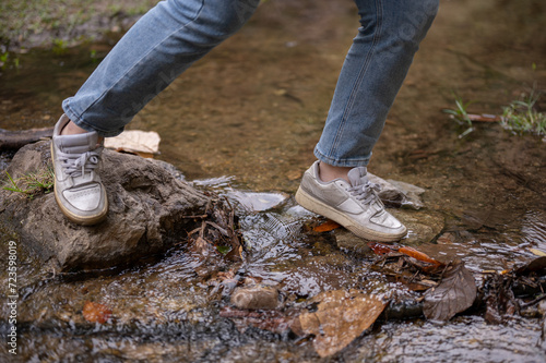 A close-up image of an adventure woman crossing a small nature canal while hiking on the mountain.