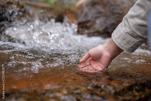 Close-up hand image of a woman touching the water in a small nature canal waterfall on the mountain