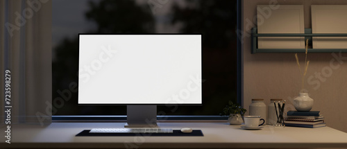 Front view of a white-screen computer mockup on a table in a modern home office at night.