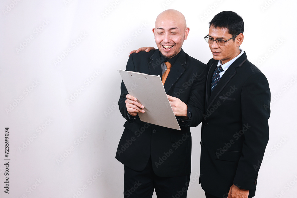 Two Asian businessmen working in team together and discussing the problem while holding clipboard Two Asian businessmen working in team together and discussing the problem while holding clipboard