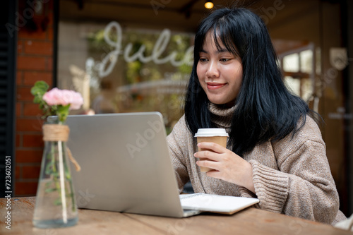 A beautiful Asian woman is working remotely at a cafe in the city, working on her laptop.