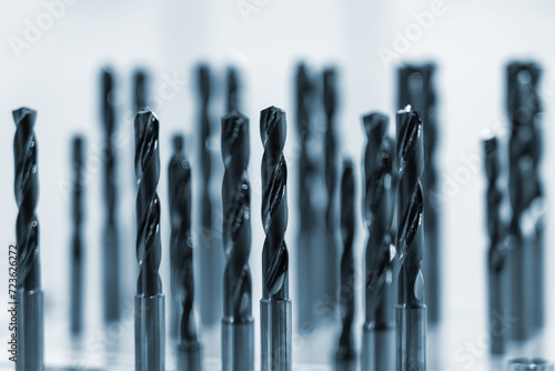 Collection of drill bits in blue hue. They are arranged in two rows in front of white background. Drills are made of metal and have spiral design photo