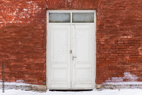 Closed outdoor white wooden door in red brick wall