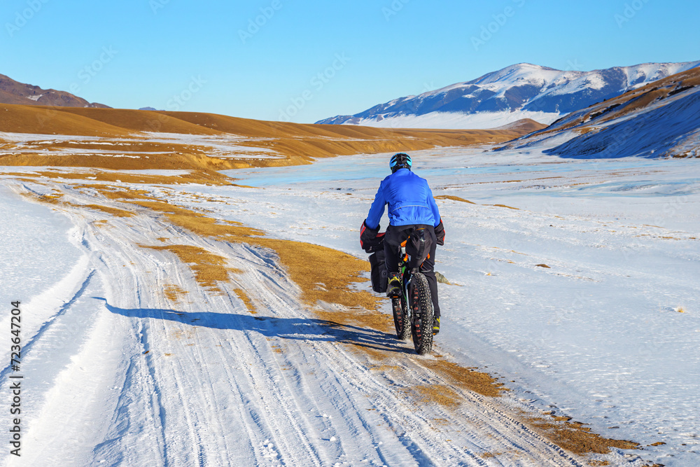 A male traveler rides a fat bike in the mountains in winter. Winter trip. High mountain plateau Turgen-Asy, Kazakhstan.