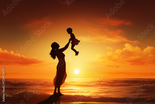 Silhouette of mother raising baby girl up high on a beautiful sunset beach 