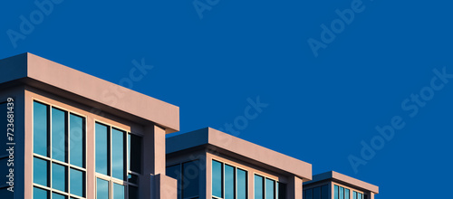 Row of modern three rental office buildings with sunlight on glass wall surface against dark blue sky background, low angle and panoramic view 