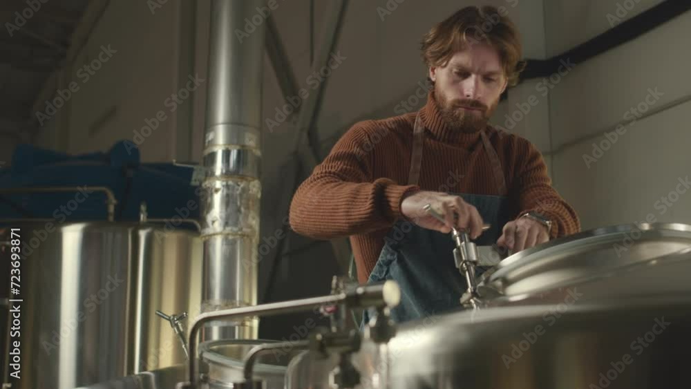 Medium shot of Caucasian male brewery specialist looking inside stainless-steel brew tank, controlling process of beer fermentation and maturation Medium shot of Caucasian male brewery specialist looking inside stainless-steel brew tank, controlling process of beer fermentation and maturation