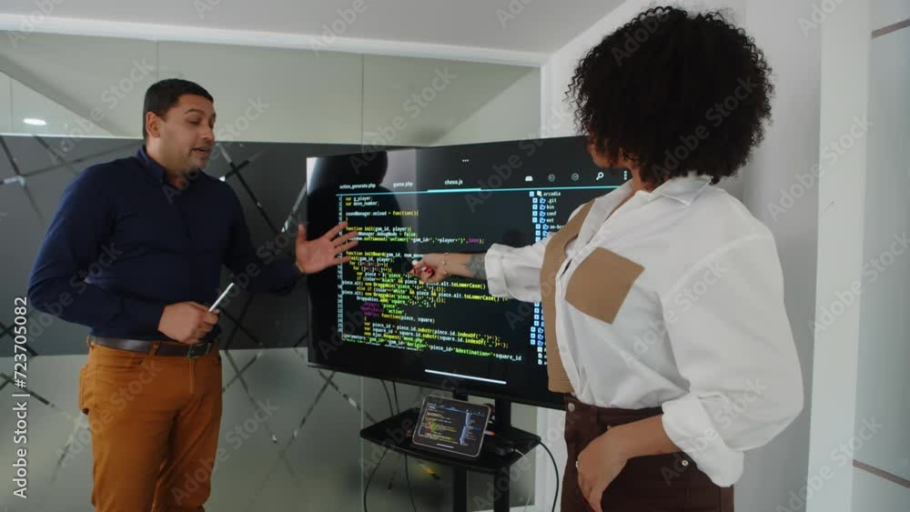 Medium shot of male developer presenting new script for app standing next to monitor and talking with female colleague Medium shot of male developer presenting new script for app standing next to monitor and talking with female colleague