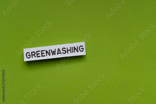Weiße Zettel mit Wort greenwashing- flach auf einem farbigen Untergrund, aus der Draufsicht fotografiert.  Notizzettel in Nahaufnahme minimalistisch