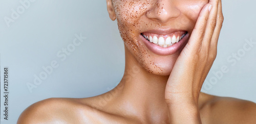 Skin care cropped beauty portrait.  Facial scrub young happy Indian or sough asian woman is posing with salt coffee peeling cosmetic product on the half of her face. Dermatology. photo