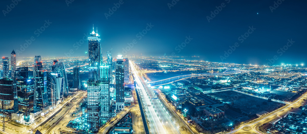 Spectacular urban skyline with colourful city illuminations. Aerial view on highways and skyscrapers of Dubai, United Arab Emirates.