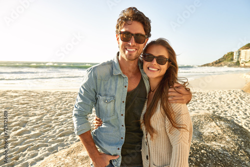 Couple  beach and sunglasses with hug  smile and care with fashion  eye protection and vacation in summer. Man  woman and embrace with glasses for sun  trendy style and together with love on holiday