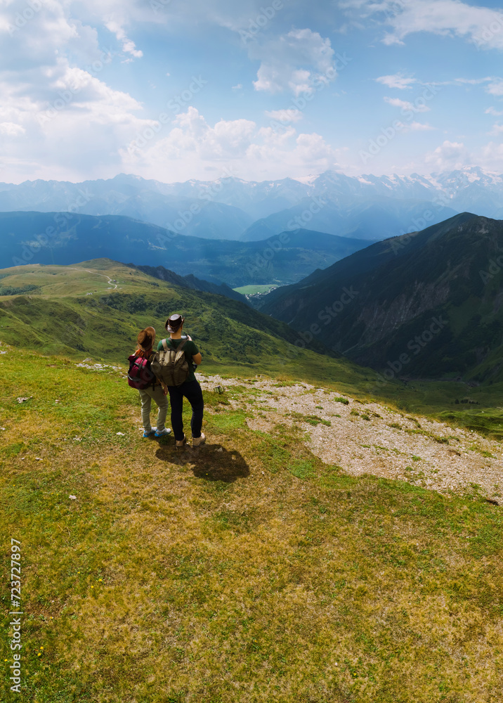 Couple woman and man wearing wide sun hat and backpack, tourists on trail to Koruldi Lakes, Mestia Georgia. The concept of travel and active recreation. Summer day. Aerial vertical photo