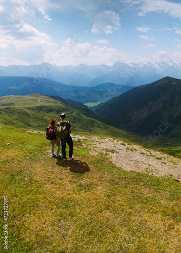Couple woman and man wearing wide sun hat and backpack, tourists on trail to Koruldi Lakes, Mestia Georgia. The concept of travel and active recreation. Summer day. Aerial vertical photo © Sergey