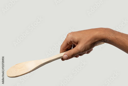 Black male hand holding a wooden cooking spoon on grey background. photo