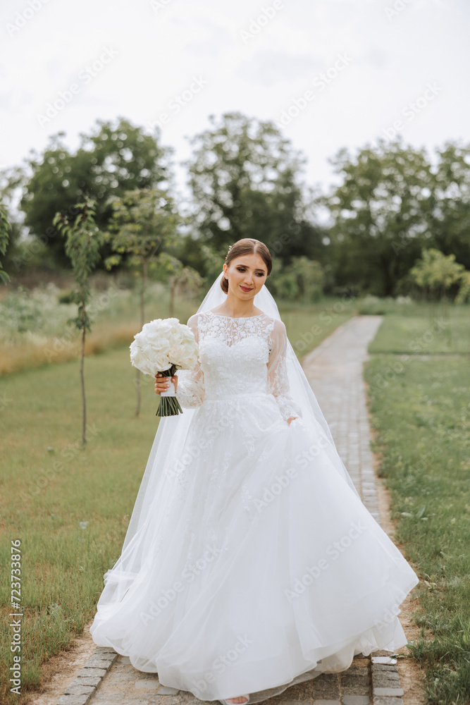 Beautiful bride with a long train. The bride in a white dress with a long train in nature on a summer day. Summer wedding.
