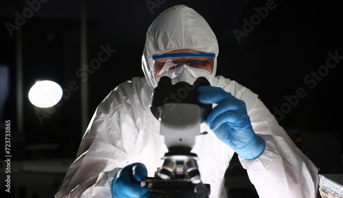 Man in protective suit looks through microscope. COVID-19 coronavirus infection. Research pathogenic bacteria. Special experiments and research. Healthcare in world. Virus test in laboratory