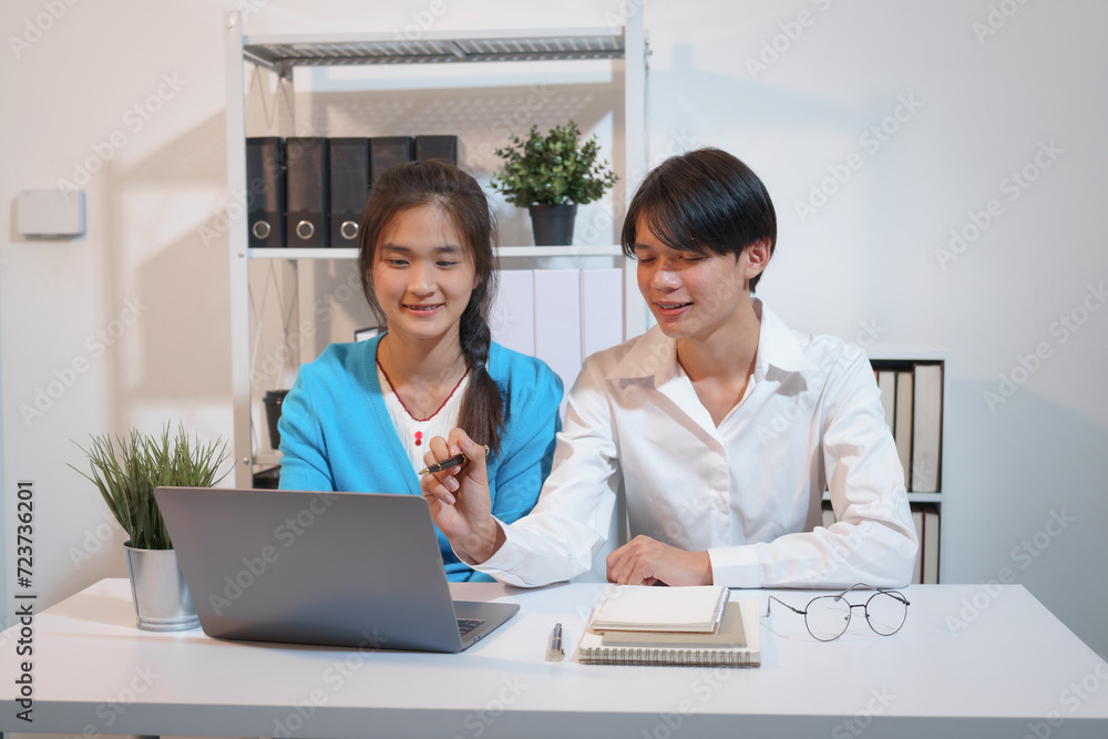 An Asian male consultant and an African American female intern sit at a table with laptops doing paperwork together to discuss a project's financial reports. Company business collaboration concept An Asian male consultant and an African American female intern sit at a table with laptops doing paperwork together to discuss a project's financial reports. Company business collaboration concept