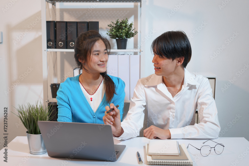 An Asian male consultant and an African American female intern sit at a table with laptops doing paperwork together to discuss a project's financial reports. Company business collaboration concept An Asian male consultant and an African American female intern sit at a table with laptops doing paperwork together to discuss a project's financial reports. Company business collaboration concept