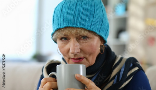 Elderly woman feels sick and drinks tea at home. Lady in knitted hat takes cup tea. Parents do not tolerate loneliness, suffer from complications. Chronic diseases, frequent concomitant aging
