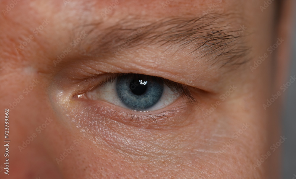 Fototapeta premium Close-up unkind angry look man, eye young man. Depression and anxiety during pandemic. Focused attention to detail. Hide true intentions. Nonverbal communication tool. Bossy stare