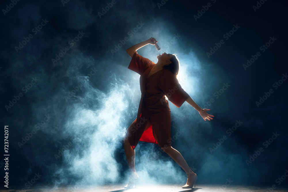 Voice Unbound. Solo artist performing live, arm extended, amidst atmospheric stage lighting and fog against black background. Concept of hobby, festival, concert, disco, entertainment. Ad