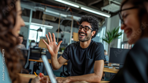 Young man with an afro hairstyle and glasses is smiling and giving a high-five in a casual office or coworking space environment. photo