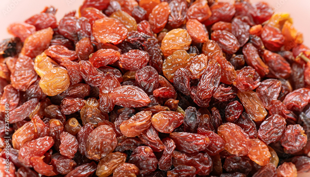 Raisins texture background, closeup, top view. Heap of dried red grapes, selective focus photo; blurred foreground and backdrop