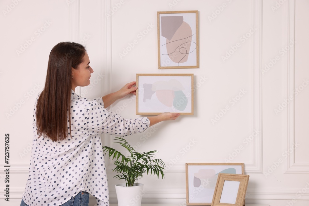 Woman hanging picture frame on white wall at home Woman hanging picture frame on white wall at home