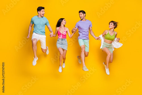 Full size photo of four fellows hold hands jump run fast enjoy free time together isolated bright color background