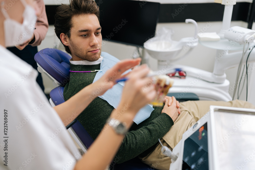 Cropped shot of unrecognizable female dentist explaining how to take care oral cavity model and teeth include dental disease to male patient, sitting on dental chair in dentistry clinic. Cropped shot of unrecognizable female dentist explaining how to take care oral cavity model and teeth include dental disease to male patient, sitting on dental chair in dentistry clinic.