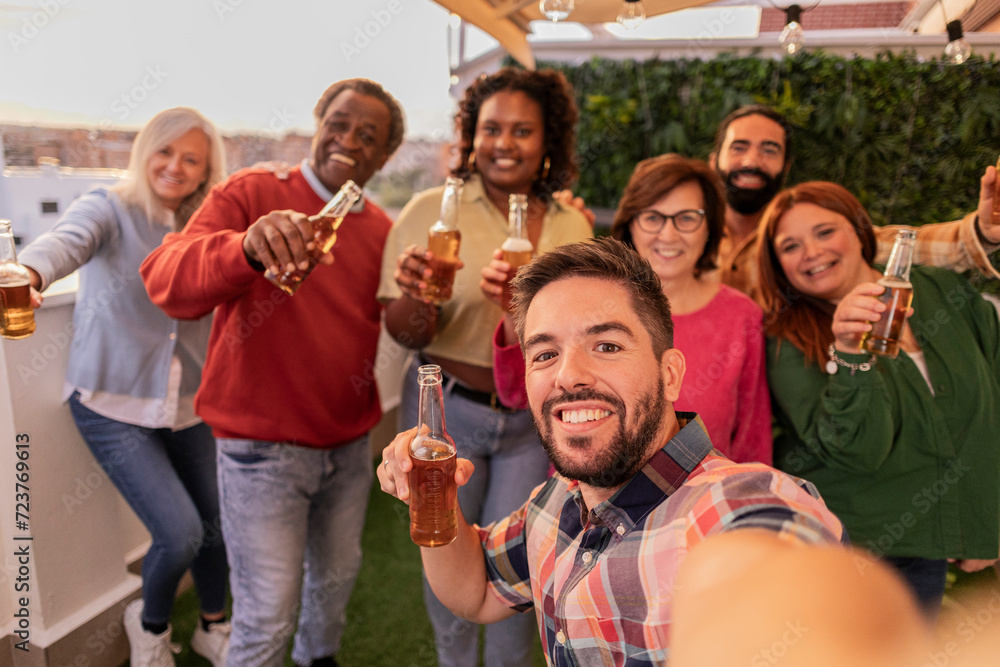 Obraz premium Group selfie of multiethnic friends on rooftop terrace toasting with beer at sunset