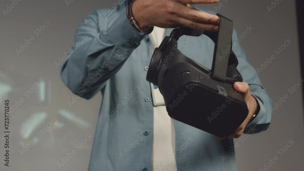 Medium close-up shot of unrecognizable male tech company executive standing on stage in conference hall during product presentation, demonstrating new model of virtual reality headset to public Medium close-up shot of unrecognizable male tech company executive standing on stage in conference hall during product presentation, demonstrating new model of virtual reality headset to public