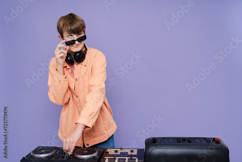 Cool charming boy with headphone and sunglasses play music on a turntable isolated over bright color background