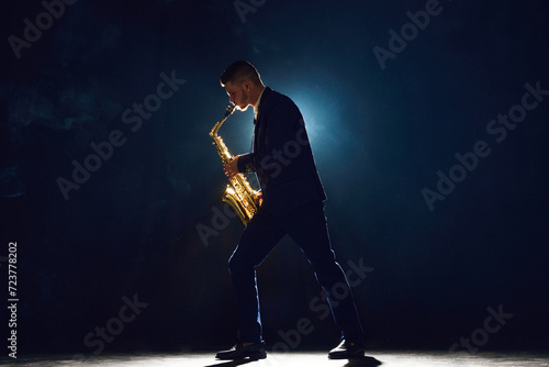 Dynamic portrait of saxophonist in formal attire passionately performing on stage with smoke under spotlights. Concept of art, instrumental music, dance, culture, festivals and concerts.
