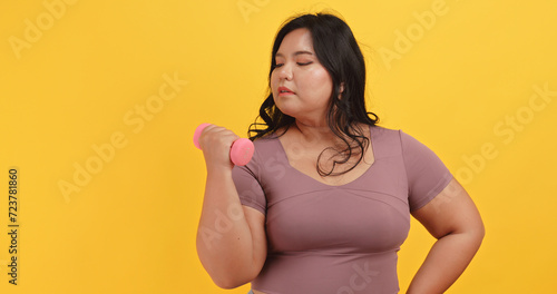 A chubby Asian woman wearing exercise clothes is showing off her physical strength on a yellow background.