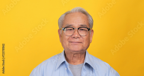 Close up, portrait of older man smiling and looking at the camera. Isolated on yellow background in the studio. © ronnarong