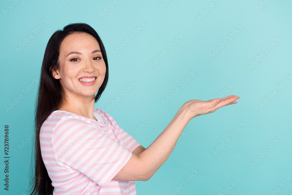 Photo of cheerful positive metis mixed race woman wear pink t-shirt showing arms empty space isolated turquoise color background Photo of cheerful positive metis mixed race woman wear pink t-shirt showing arms empty space isolated turquoise color background