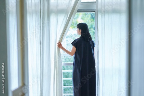 Obraz w ramie レースカーテンを開けて窓から外を見る若い女性