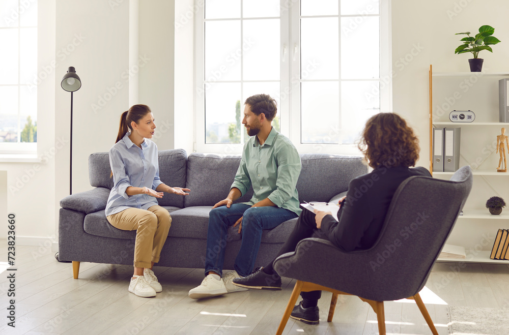 Young couple talking about marriage problems sitting at family therapist office during therapy session. Male psychologist listening his patients trying to find solution. Mental health concept Young couple talking about marriage problems sitting at family therapist office during therapy session. Male psychologist listening his patients trying to find solution. Mental health concept