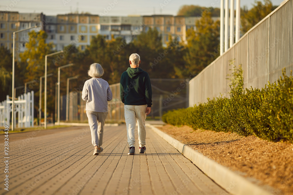 Senior retired couple wearing sportswear walking along a path in the park having sport workout. Elderly men and women exercising outdoors. Workout in nature and healthy lifestyle concept.