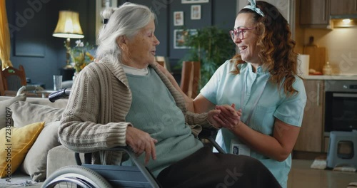 Senior woman in wheelchair and nurse caregiver with holding hands, talking, support and care in retirement at home photo
