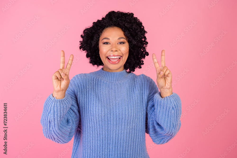 Photo portrait of attractive young woman show double v-sign dressed stylish blue knitted clothes isolated on pink color background Photo portrait of attractive young woman show double v-sign dressed stylish blue knitted clothes isolated on pink color background