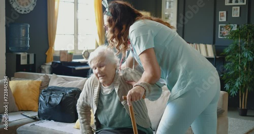 Nurse assisting senior grandmother in walking at home. Old woman has a problem with her legs and it is difficult to walk, she feels faint while standing up with the help of a caregiver photo