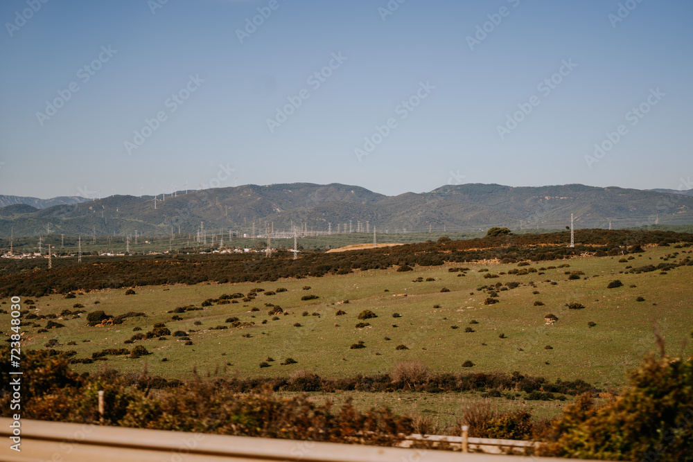 Santa Margarita, Spain - January 24, 2024 -  landscape with green fields, wind turbines, and mountains in the background under a clear blue sky.