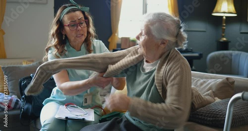 A nurse or caregiver helps an elderly female patient to get dressed at home. Service of providing assistance and care to elderly people at home
